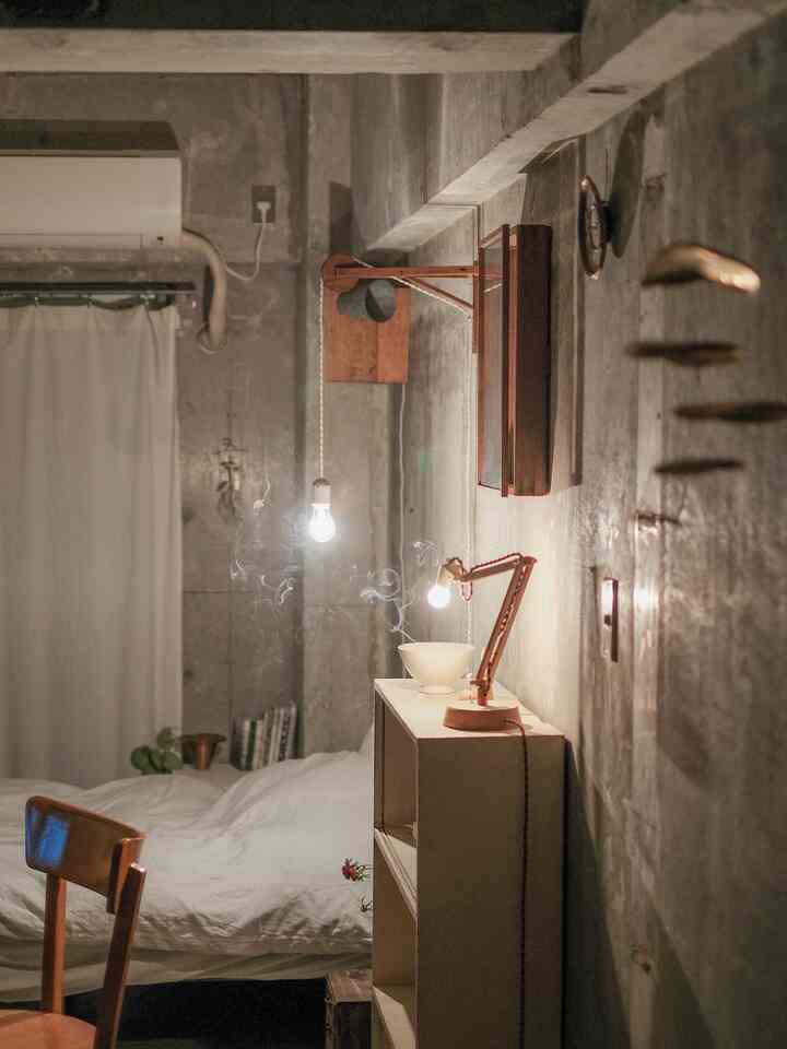 白とグレーのモノトーンでまとめられた狭い寝室に、木製家具と間接照明が配置された落ち着いた雰囲気のインテリア