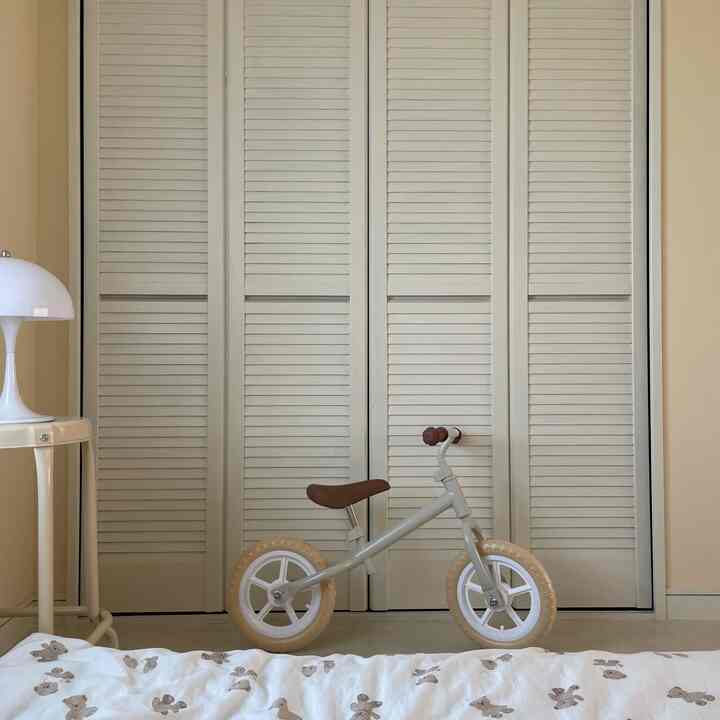 Beige-toned kids' room with a small balance bike centered and a white table lamp on the side, showcasing a simple and natural space