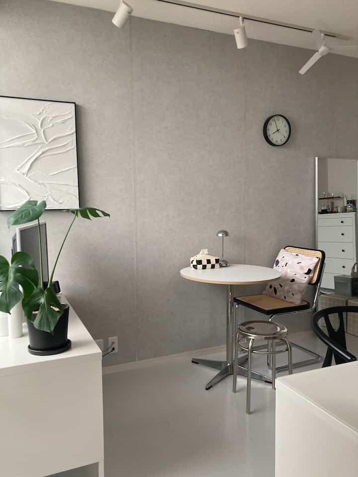 白とグレーの色調の狭い部屋、丸いテーブルとスツール、植物が配置されたモダンなおうちカフェのインテリア