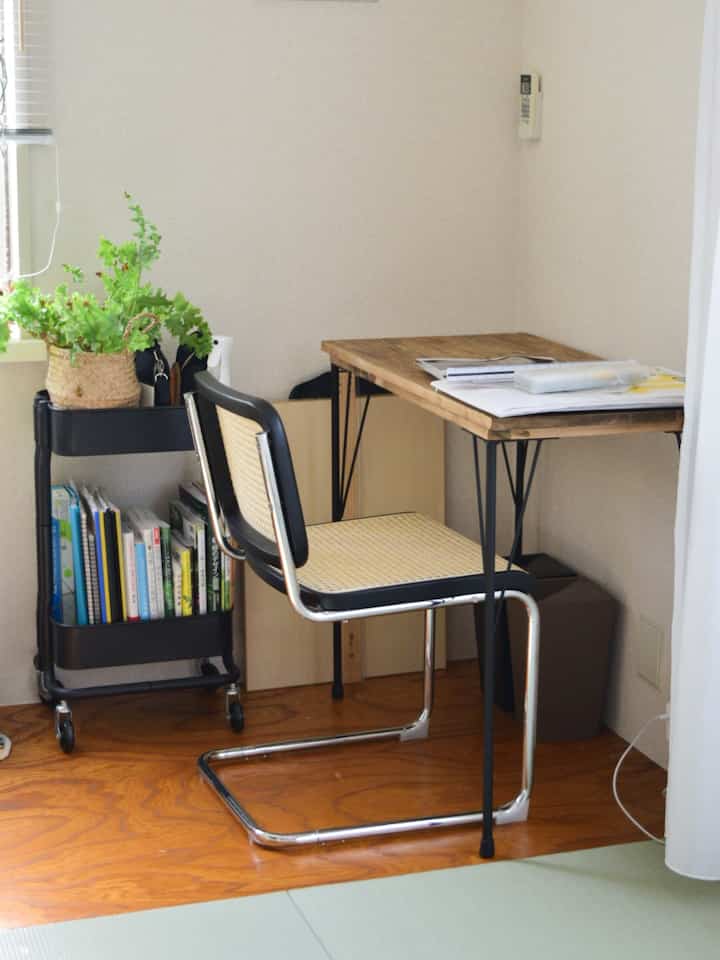 ベージュの壁と木目調の床があるホームオフィス、ミッドセンチュリーモダンのデスクとラタンチェアが配置された雰囲気のある作業空間