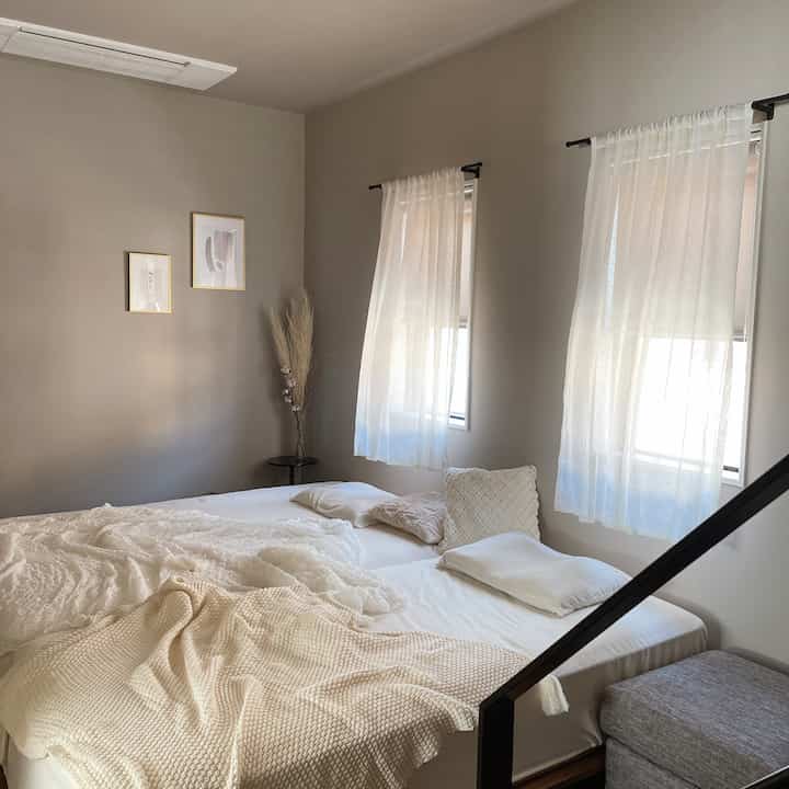 Beige and white toned bedroom with white bed and pillows, sheer curtains creating a soft natural atmosphere