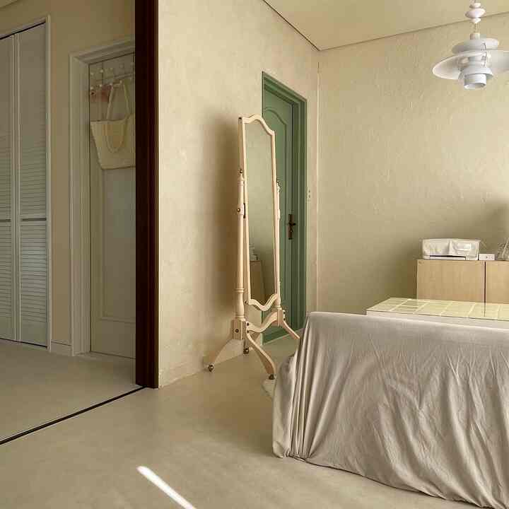 ベージュとナチュラルな色調の寝室とリビングの境目の空間、全身鏡とベッドカバーが配置された温かみのあるインテリア