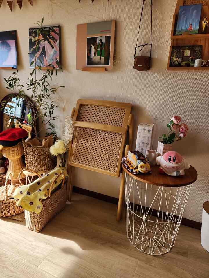 ナチュラルカラーの落ち着いたリビングの一角、ラタン製の折りたたみ椅子とワイヤー脚のサイドテーブルが配置された雰囲気のある空間