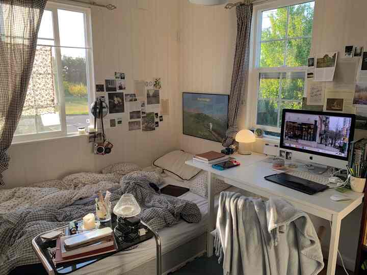 Natural color compact bedroom for single household featuring a desk workspace with monitor and decorated walls, illuminated by soft daylight