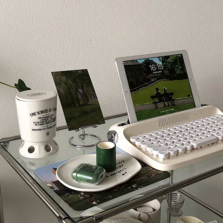 A white and green toned home office corner featuring a vintage-style keyboard, candle, and plant, creating a calm ambiance
