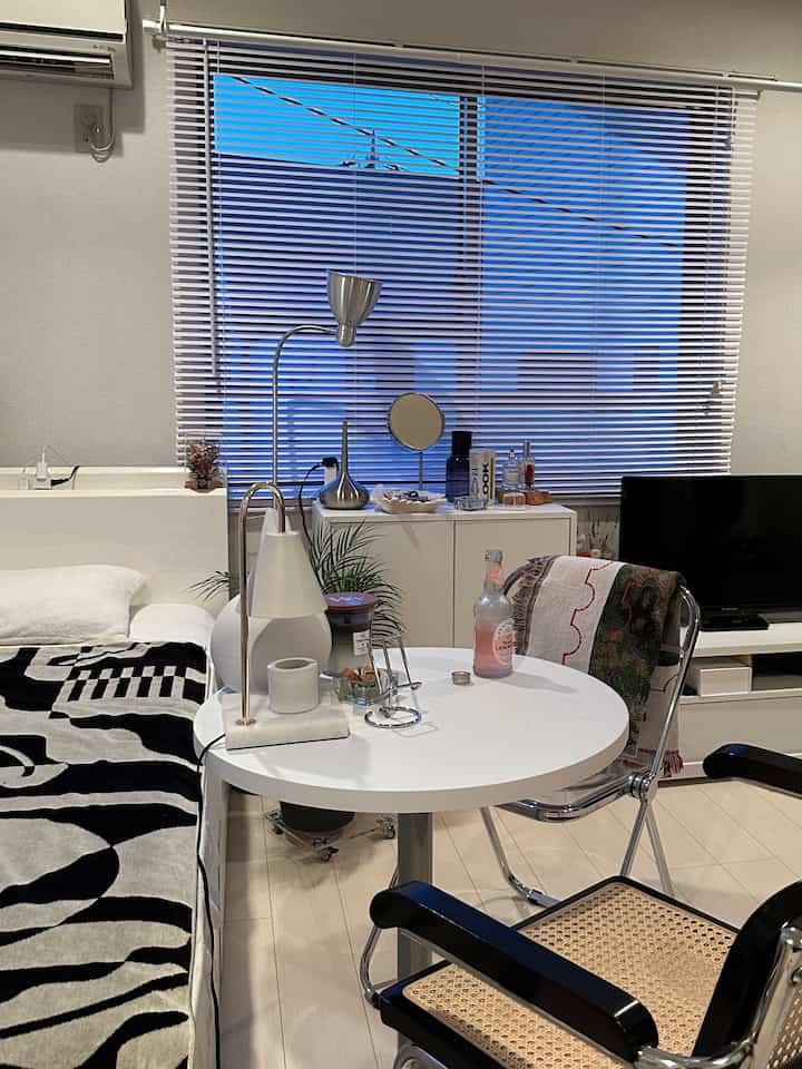 White-toned single household living room featuring a round side table with a lamp, cane chair, and black-and-white rug creating a cozy atmosphere