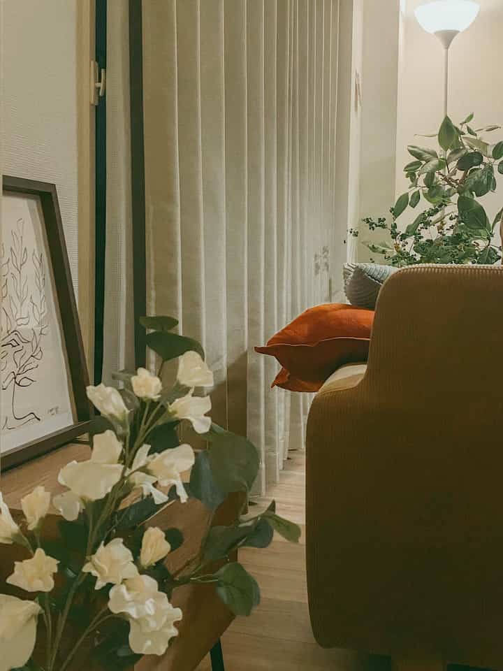 ブラウンとグリーンの色調の1LDKリビング、クッションや植物が配置された雰囲気のある自然モダンな空間