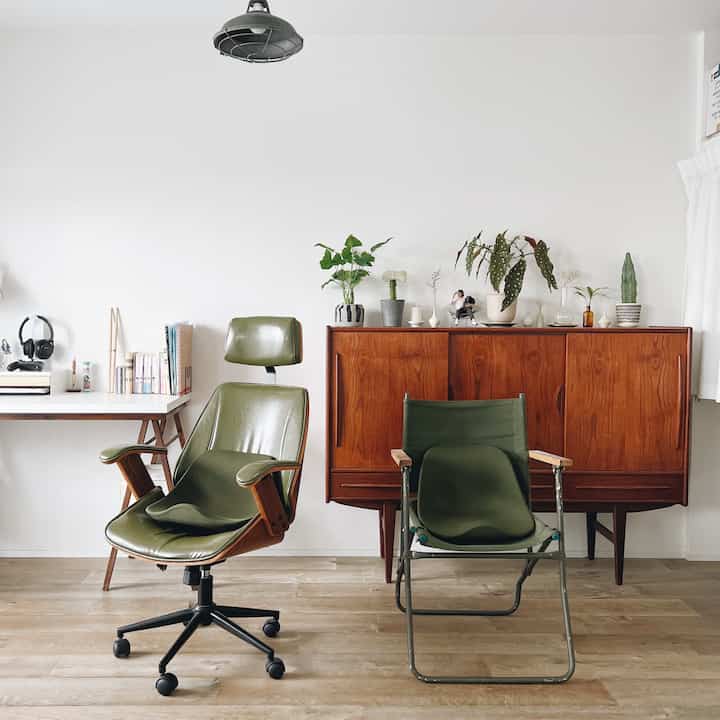 白い壁と木目調家具、緑色のハイバックロッキングチェアが配置されたナチュラルモダンなワークスペース