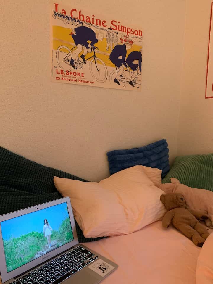 A studio apartment space featuring a peach pink bed with assorted colorful cushions, creating a warm and cozy atmosphere