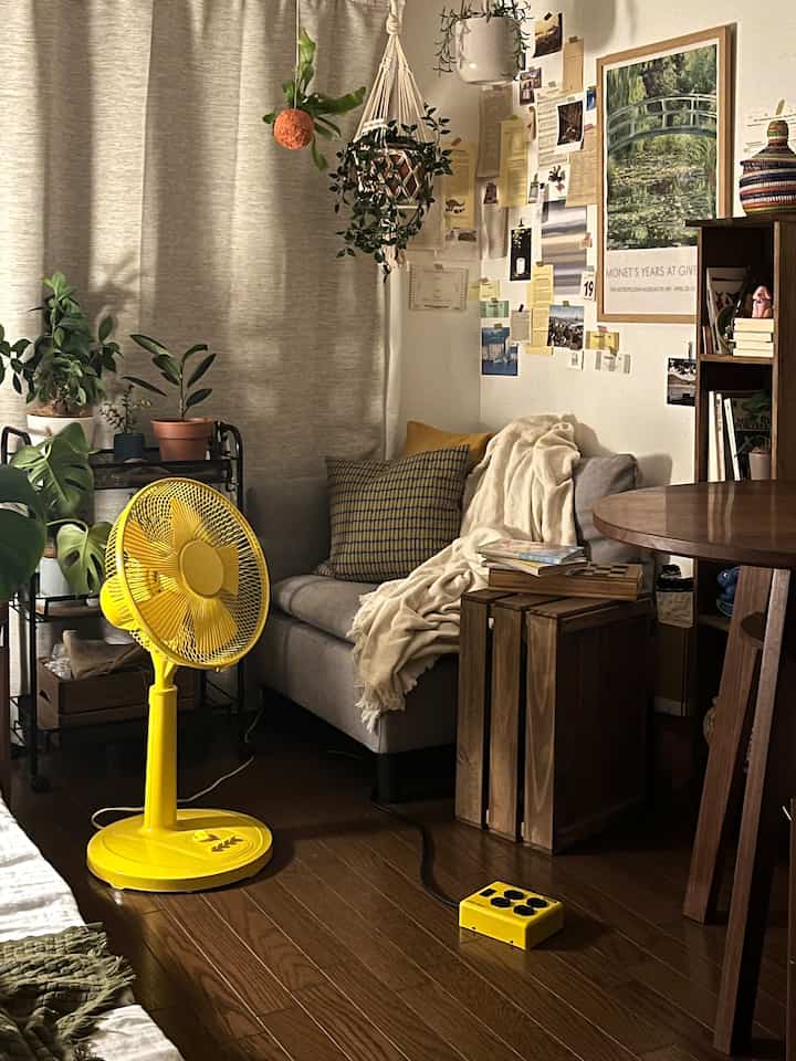 Cozy small studio room in warm beige and brown tones featuring a gray sofa and vibrant yellow fan