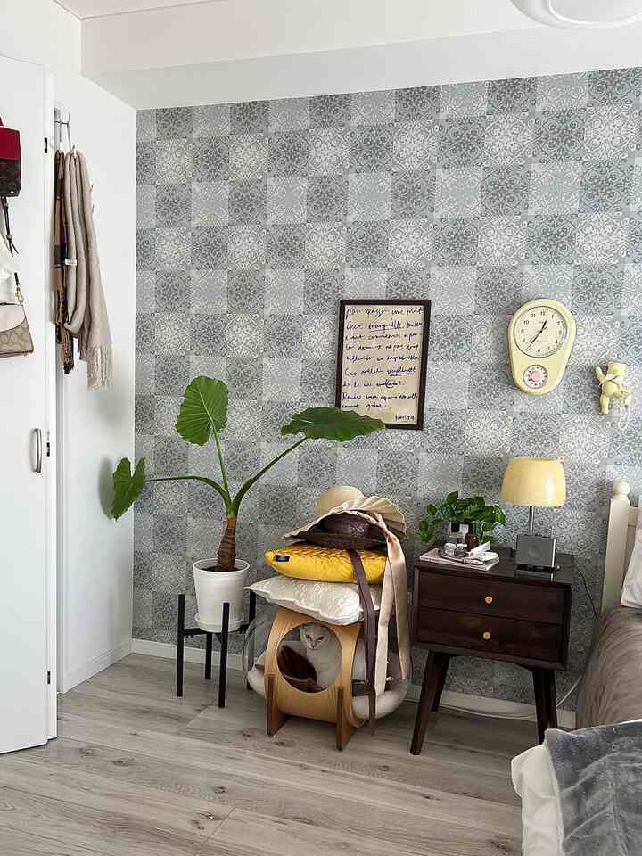 グレーの模様壁紙と木目調のナイトテーブル、透明なペットベッドが配置された雰囲気のある寝室