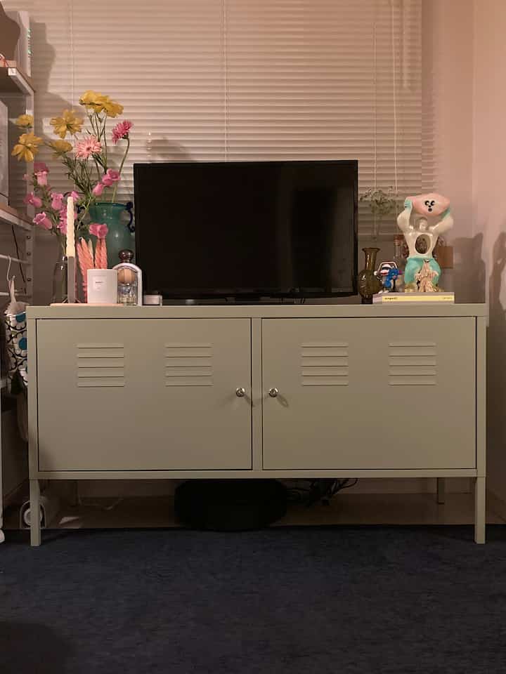 黄色のトーンのリビング、中央にIKEA PSキャビネットとテレビ、花瓶や照明が配置されたモダンな空間