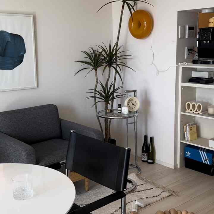 White and gray toned living room featuring a gray sofa, round table, green plants, and yellow wall objet with a clean aesthetic
