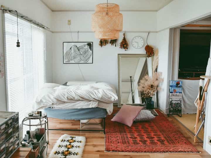 Cozy natural-tone bedroom featuring a large red rug and silver mirror in a simple setting