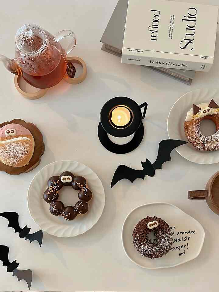 White table featuring multiple donuts, a tea pot, and a lit candle creating a cozy home cafe atmosphere