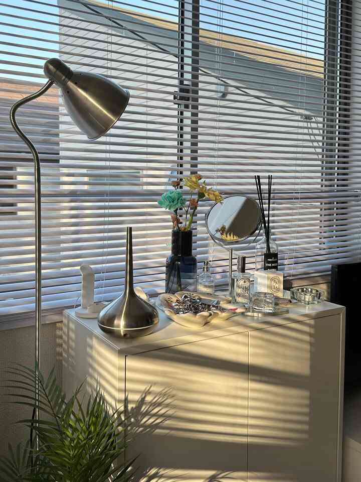 Indoor space bathed in natural light featuring a white cabinet with various decorative items and a metallic floor lamp