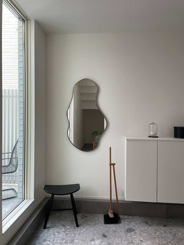 ナチュラルカラーの玄関空間、独特な形の鏡と黒いスツールが配置された印象的なインテリア