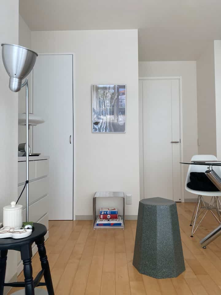 白い壁と木目調の床のミニマルなリビング、ファセットグリーンのスツールと黒いサイドテーブルが配置された空間