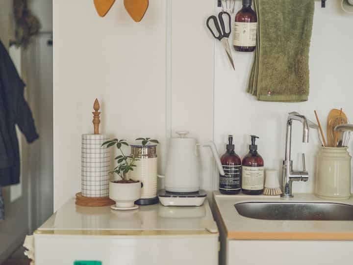 白とナチュラルな色調のキッチン、シンクとキッチン用品が整えられた清潔感のある雰囲気の空間