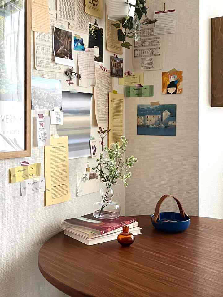Natural tone small room with wood round dining table featuring vase and books, wall decorated with photos and notes