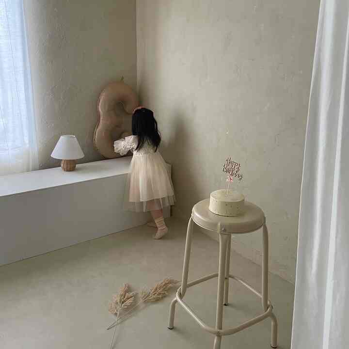 Beige-toned kids' room featuring a stool with birthday cake, white curtains, and natural warm ambiance