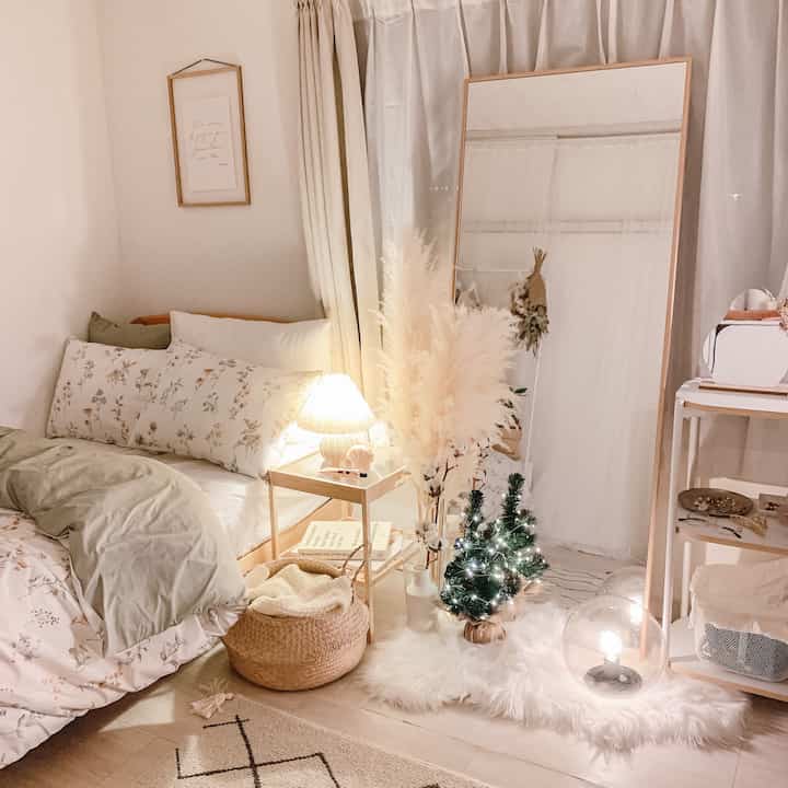暖かいベージュとアイボリーの色調の寝室、大きな鏡とナイトテーブル、ミニクリスマスツリーが配置された雰囲気のあるインテリア