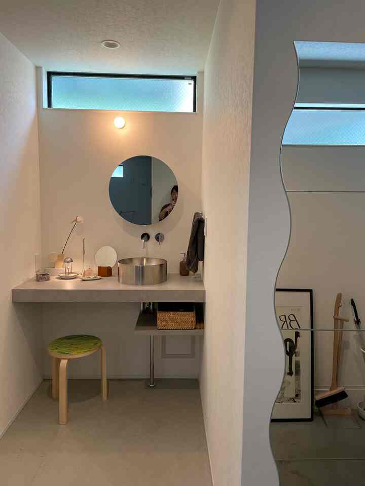 White and natural-toned entrance area with custom wash basin, round mirror, and stool arranged in a clean natural space