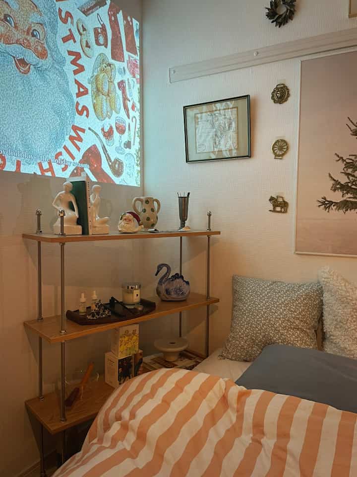 Small bedroom with wood tone shelving and cozy bedding, Christmas decorations and wall art adding a warm ambiance