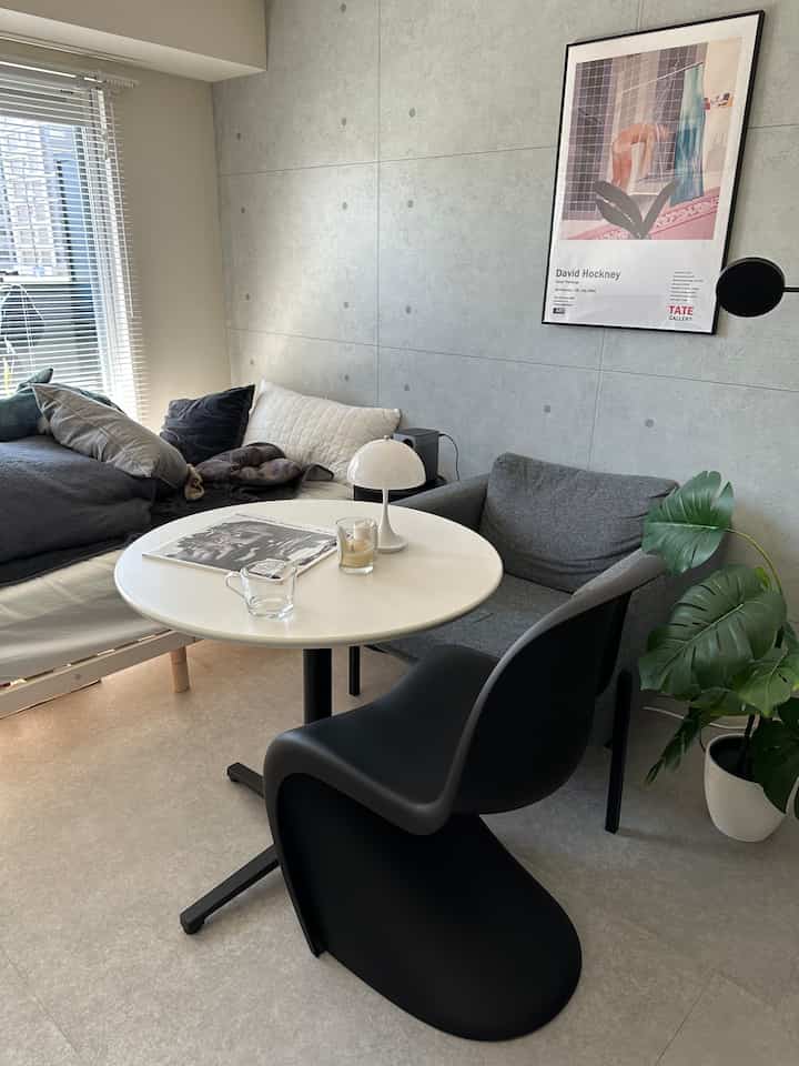 Minimal studio apartment living room with gray concrete wall, white round dining table, black chair, and gray sofa