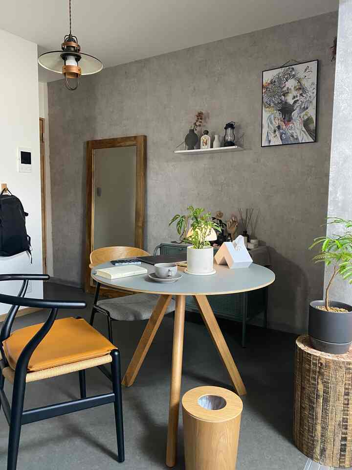 ナチュラルな色調のダイニング、丸テーブルと木製椅子、植物と壁飾りが配置された落ち着いた空間