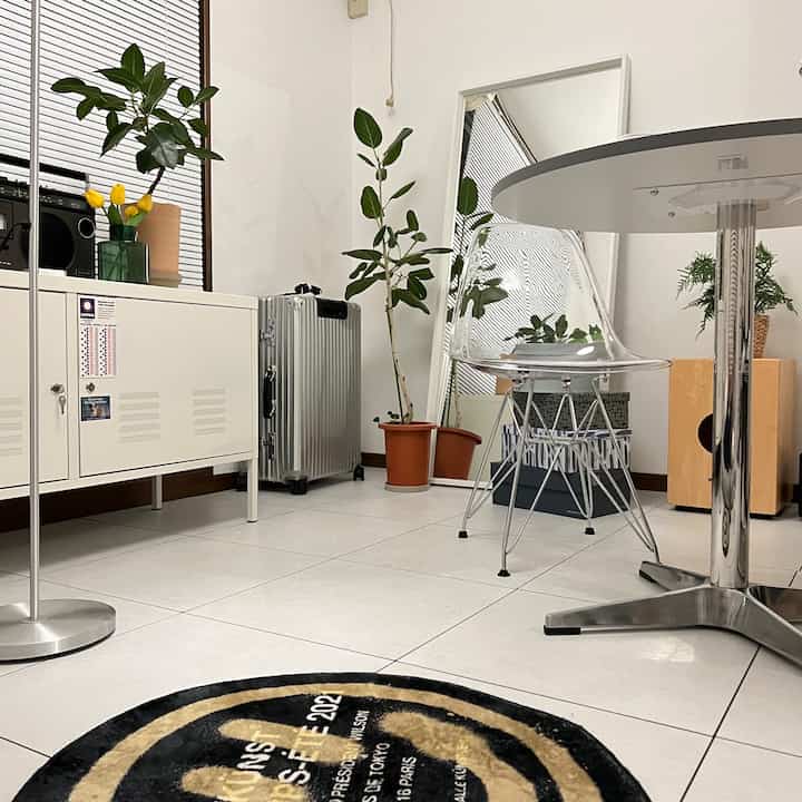 白を基調としたダイニングルーム、透明な椅子と白い金属製キャビネット、緑の植物が配置された清潔でモダンな印象の空間