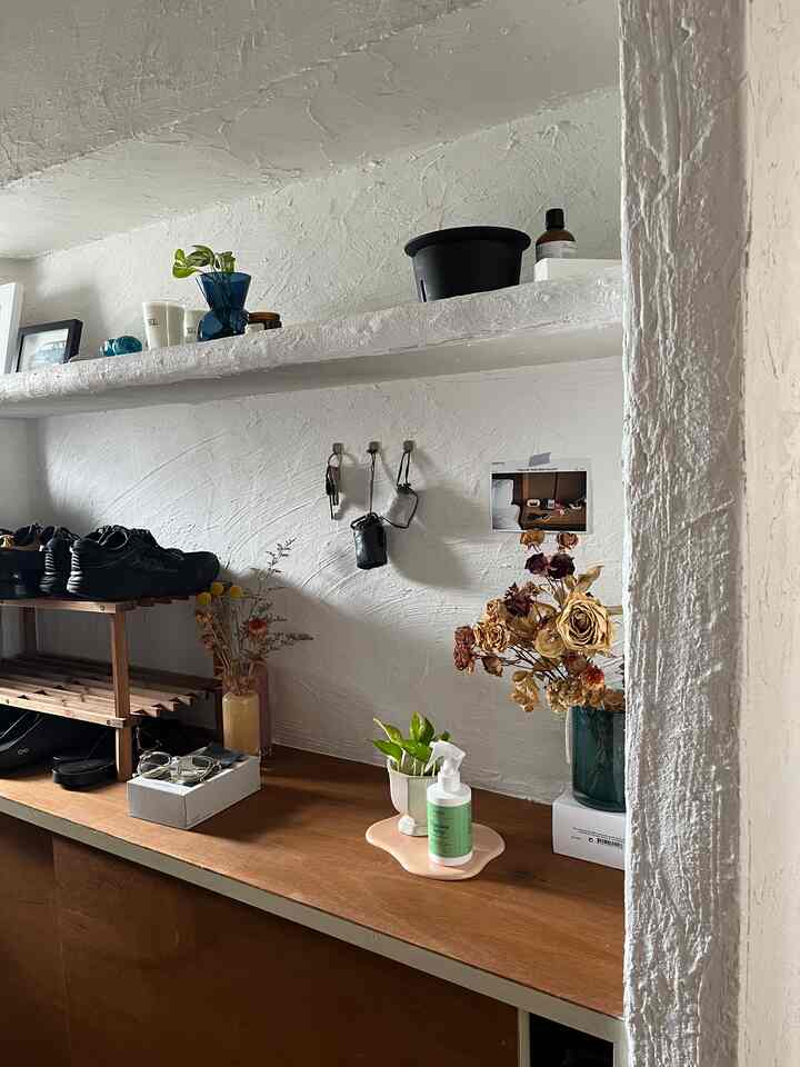 白いテクスチャ壁と茶色の木製棚、トレイが配置された静かな玄関のインテリア