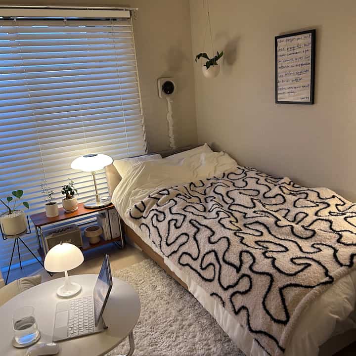 暖かいベージュと白の色調の寝室、自然素材の家具と植物、居心地の良いブランケットと照明が配置された雰囲気のあるインテリア