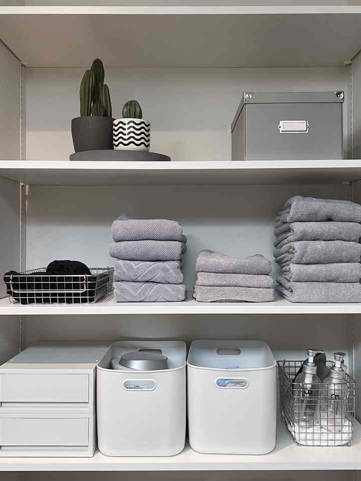 グレーと黒を基調とした脱衣所収納、タオルとポリエチレンケースが整然と並び、ホテルライクな印象的な空間