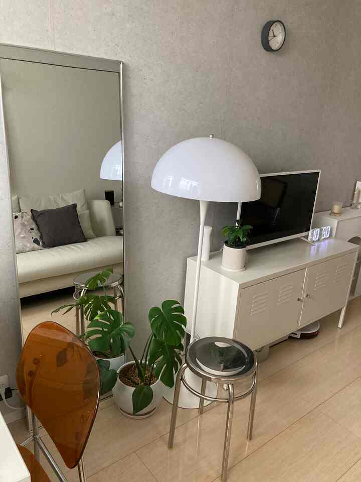 白とシルバーの色調のリビング、全身鏡とキャビネット、スツール、フロアランプが配置されたシンプルなインテリア