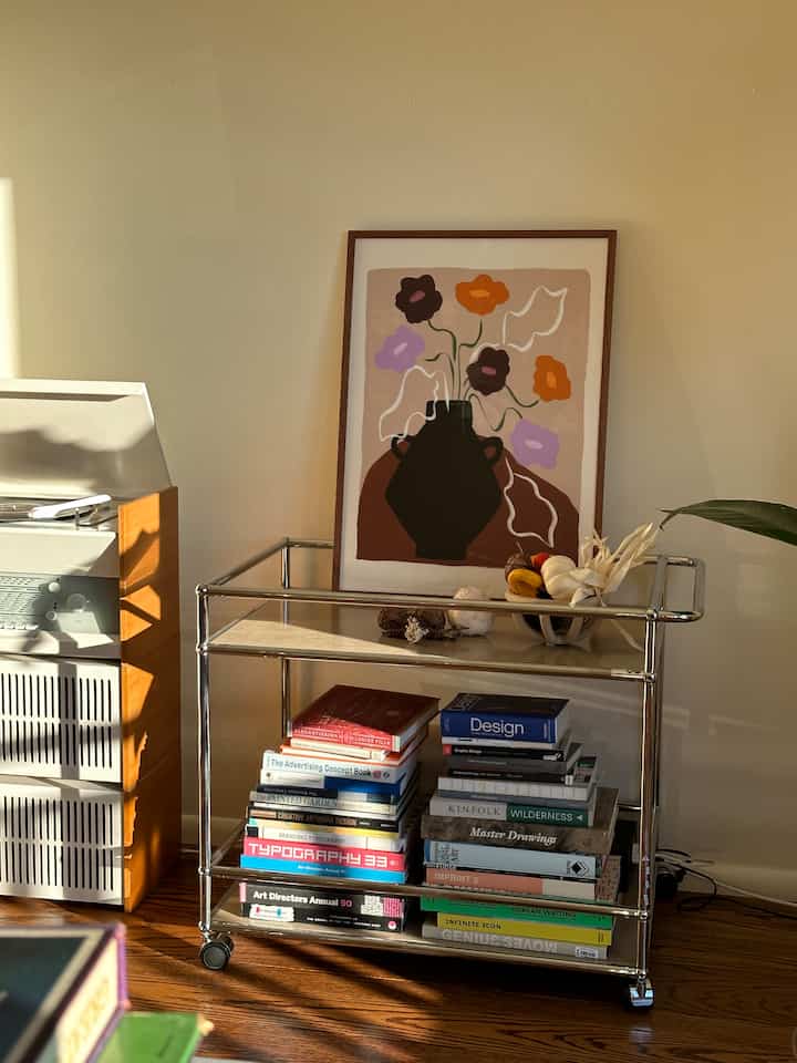 White-toned living room with wood floor featuring a mid-century modern kitchen cart neatly stacked with books and art decor