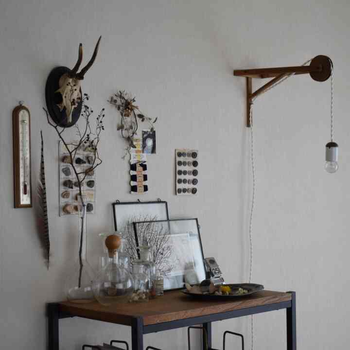 ナチュラルカラーと木目調が調和する小さな部屋、棚の上に飾られたオブジェとペンダントライトが配置されたシンプルなインテリア