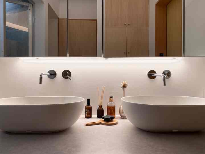 白と木目調のバスルーム、2つの洗面台とすっきりした照明が配置されたモダンな空間