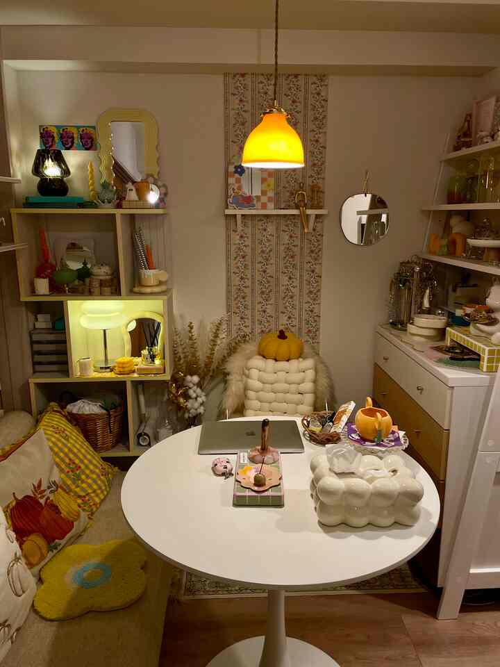 黄色とオレンジのトーンが調和する1LDKのリビングの一角、丸いテーブルとベージュのソファにカラフルなクッションや小物が配置された印象的な空間