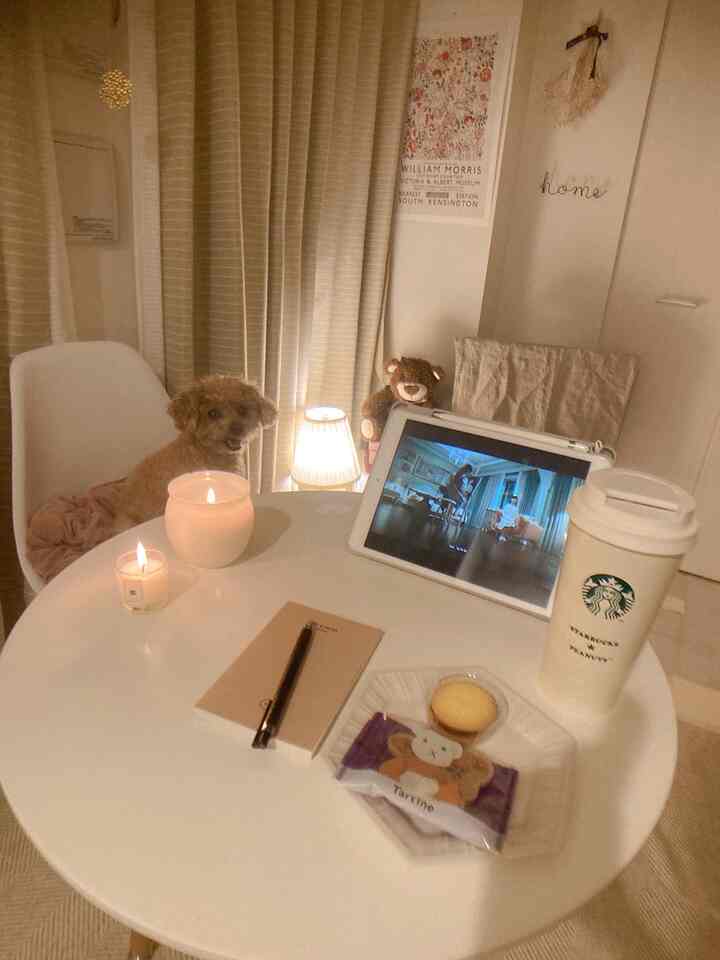 White and beige toned home cafe space featuring a table with a small dog, candles, tablet, and drink in a cozy atmosphere