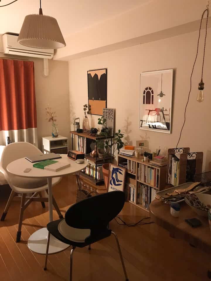 Beige and brown toned dining room featuring a round table with varied chairs, bookshelves, and posters creating a modern and natural atmosphere