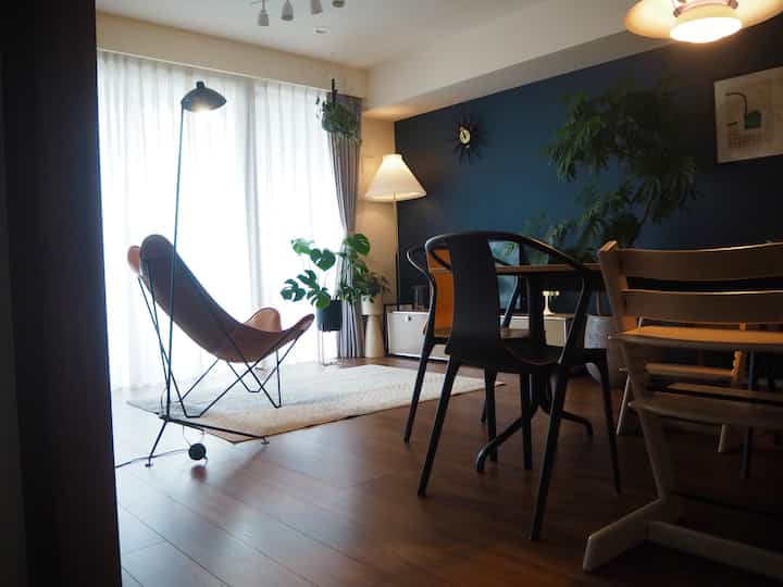 A natural modern living room with navy accent wall and wood tone flooring, featuring an armchair and floor lamps creating a cozy reading nook