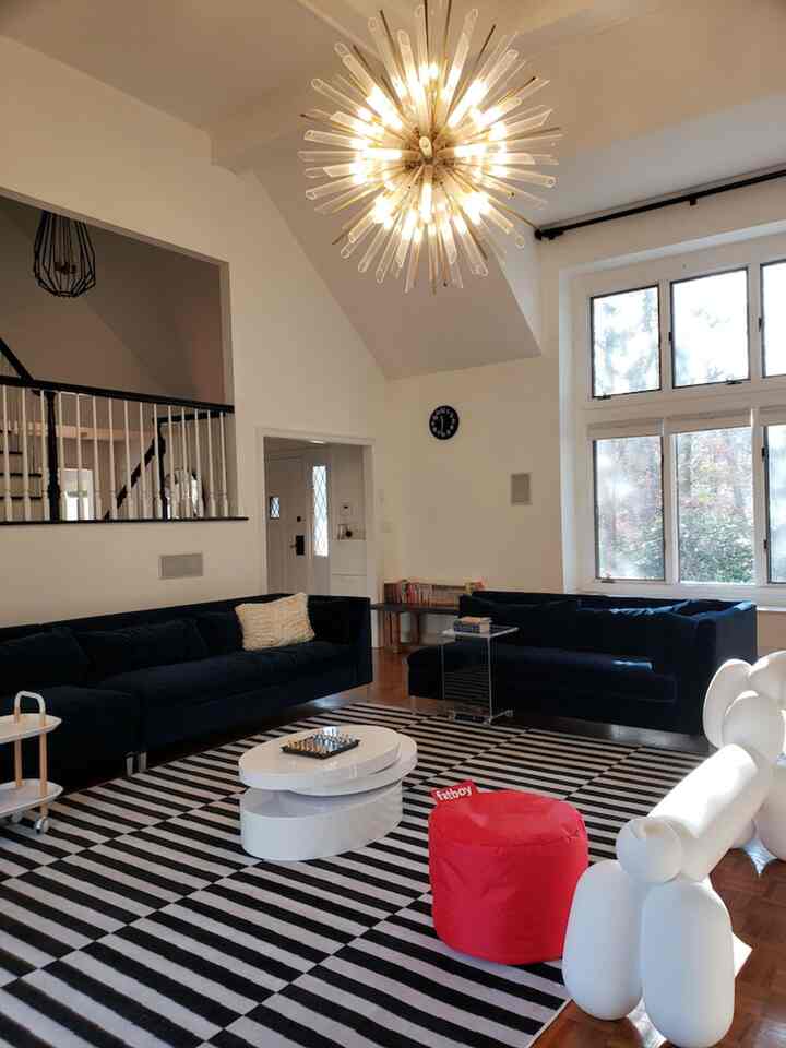 Modern living room in white and black featuring large sofas, striped rug, and a red ottoman creating a cozy atmosphere