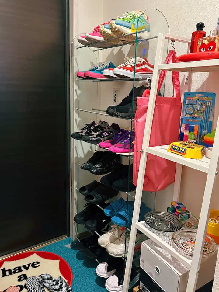 Narrow and tidy entrance featuring white shelving and shoe rack, with blue carpet flooring as background