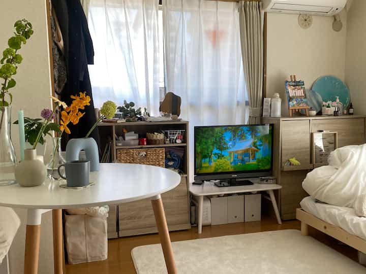 Natural color-toned studio bedroom featuring a bed, TV stand, and round table creating a cozy, simple atmosphere