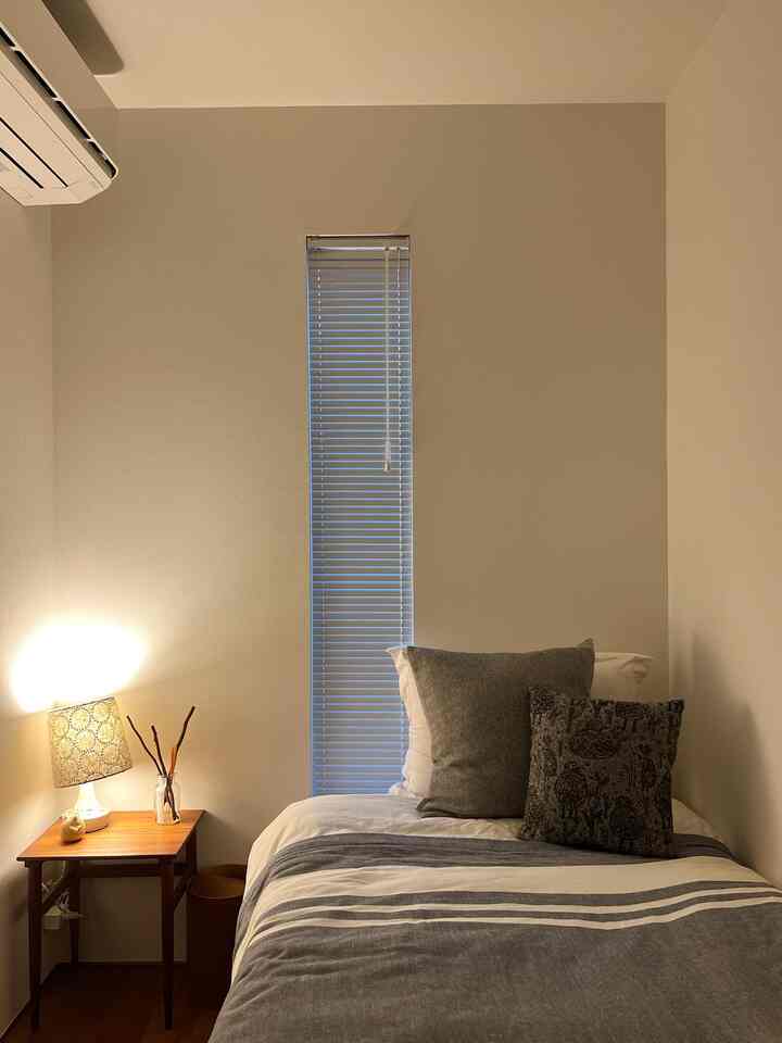 白とウッドトーンの落ち着いた寝室、シングルベッドとテーブルランプが配置されたシンプルでホテルライクなインテリア