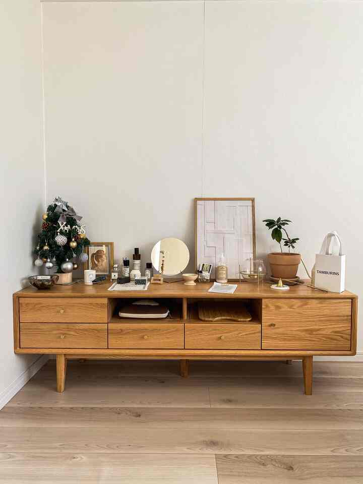 ナチュラルカラーの寝室、木目調のテレビ台上に額縁とクリスマスツリーが配置された清潔感のある空間