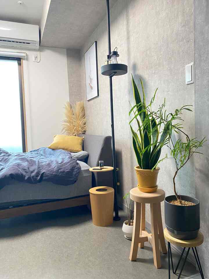 グレーとブラウンの色調の寝室、ベッド脇に植物とスツールが配置された自然な雰囲気のインテリア