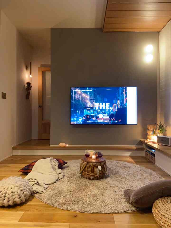 ナチュラルなウッドトーンのリビング、ラタンのバスケットテーブルとキャンドル、壁掛けテレビが配置された居心地の良い空間