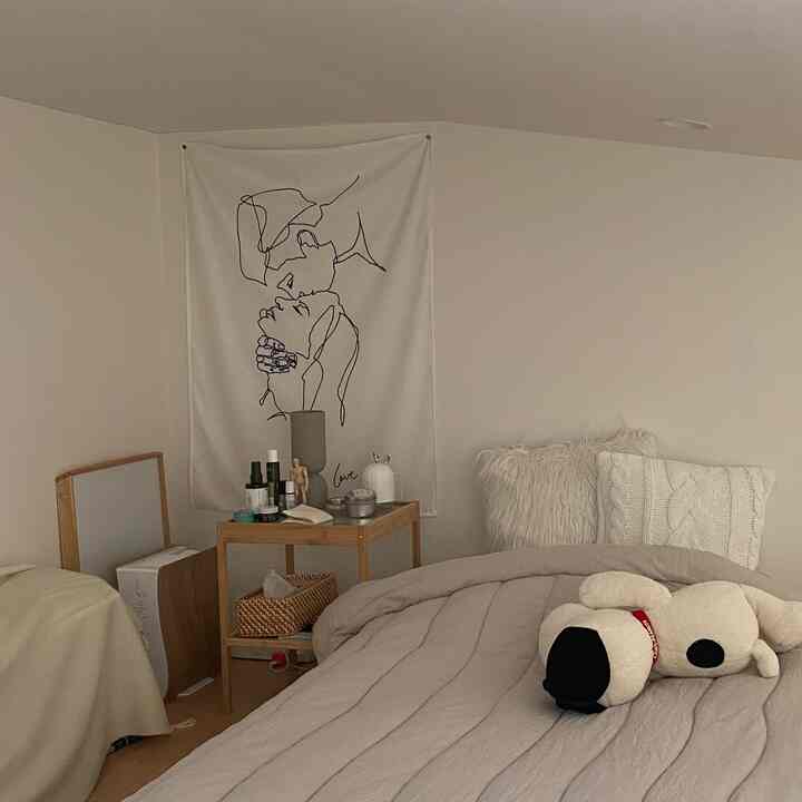 ベージュとナチュラルトーンの寝室、クッションとぬいぐるみのある快適なベッドと、スキンケア用品が置かれたサイドテーブルが配置された雰囲気あるインテリア